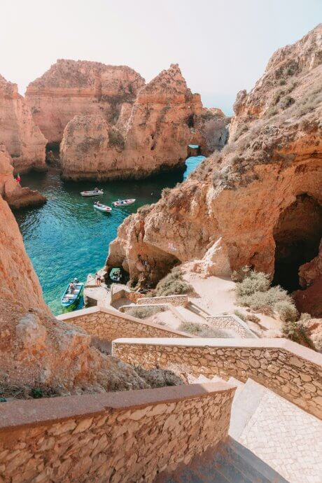 Rocky outcroppings and deep teal water with small boats in it in the Algarve, Portugal